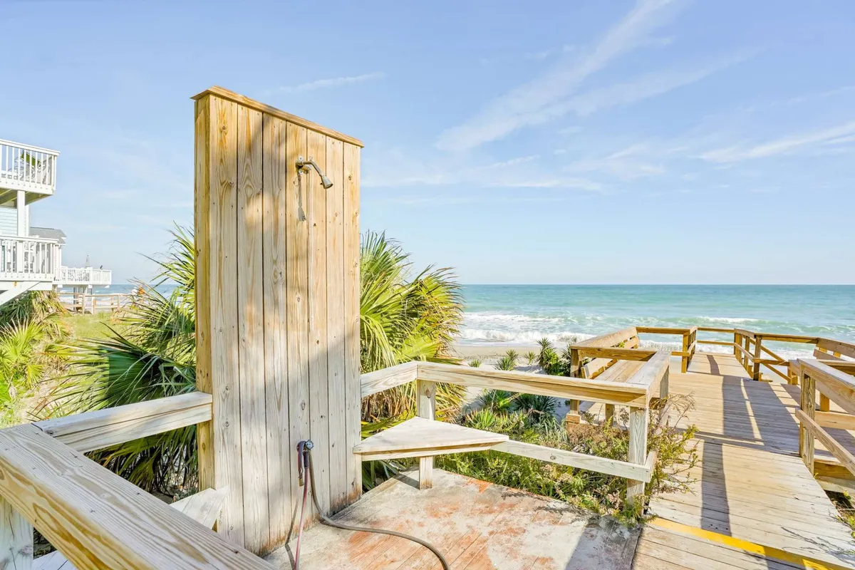 An exterior image showcasing an outdoor shower, wooden walkway, palm trees, and the ocean beyond. The tranquil scene is perfect for post-beach relaxation and enjoying sunset views.