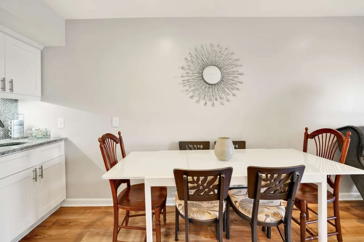 A stylish dining area with a wooden table surrounded by matching chairs, accented by a decorative mirror and beach-inspired décor. The space is bathed in natural light, creating an inviting atmosphere ideal for family meals, celebrations, or casual conversations. The setup suggests a space where stories and laughter are shared, reinforcing the communal aspect of the home's design.