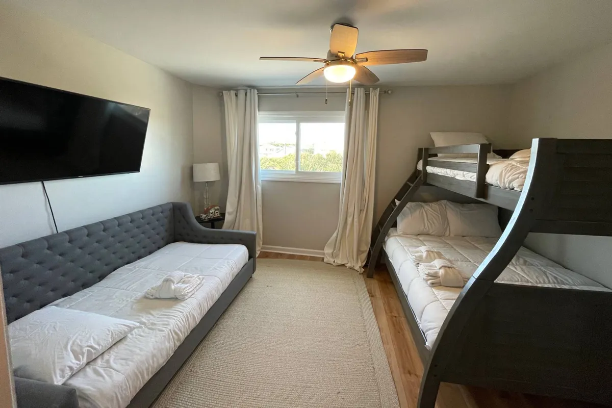 A whimsical bunk room featuring a twin-over-full bunk bed, a separate sofa bed, curtains, and a ceiling fan. The room is playful yet relaxed, making it ideal for children or families seeking an inviting sleep and play space.
