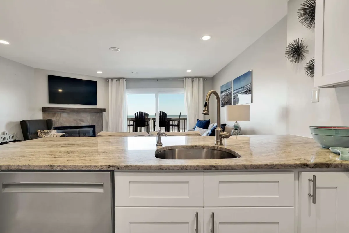 An inviting kitchen and living space with a kitchen island, modern sink, a large window letting in natural light, and comfortable seating nearby. The open layout is ideal for cooking, entertaining, and enjoying meals together, with easy sightlines to the living area.