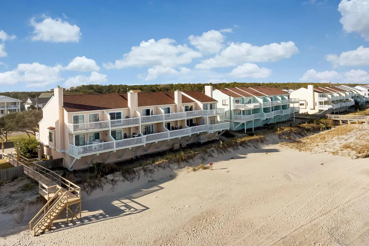 This image shows a beachfront property with multiple balconies overlooking the ocean, a wooden staircase leading directly to the sand, and a broad view of the beach. The scene is serene and inviting, with space for families to gather, enjoy walks, or just relax by the water.
